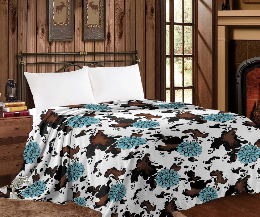 Mia Throw Blanket in Conchos Cowprint with turquoise conchos on a bed in rustic room.