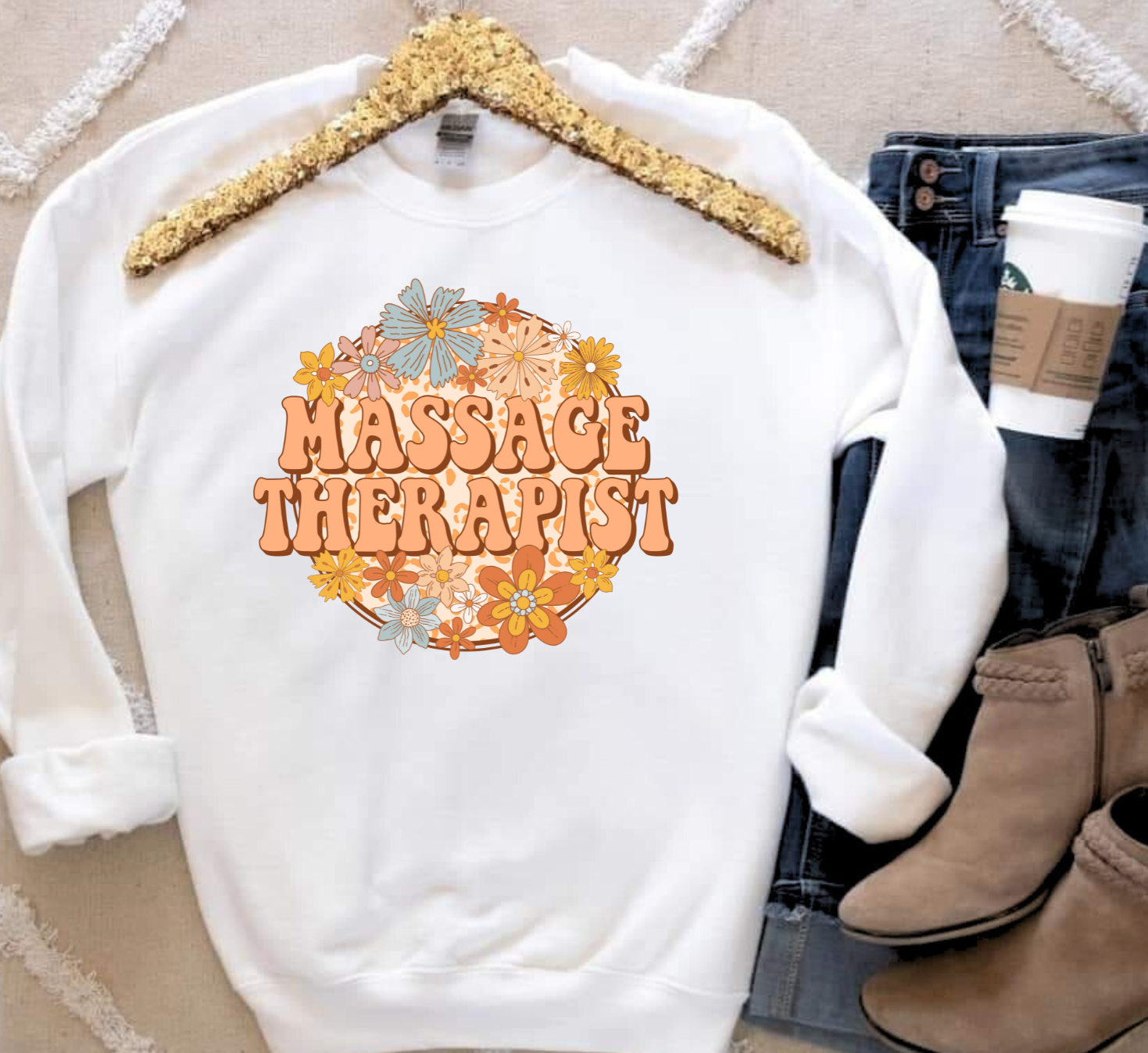 Massage Therapist shirt with floral design on a white sweatshirt, styled with jeans and boots.