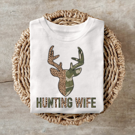 Hunting Wife camo shirt with deer head design on wooden background.