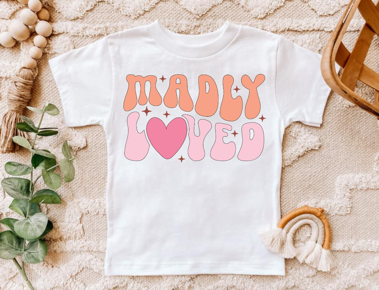 Madly Loved Pink infant and toddler shirt on textured background.