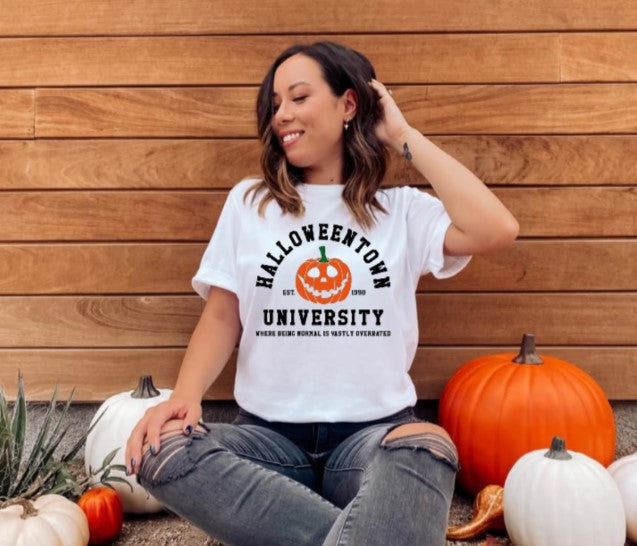 Halloweentown University Tshirt with pumpkin design worn by person, surrounded by pumpkins.