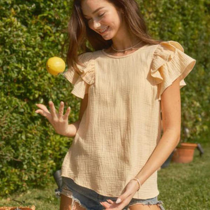 Short ruffle sleeve tunic blouse with a relaxed fit, worn by a woman outdoors.