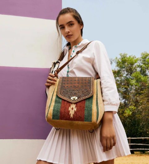 MYRA- Embossed Scarlet hand-tooled bag with vibrant colors, upcycled from a rug, worn by a model in a white dress.