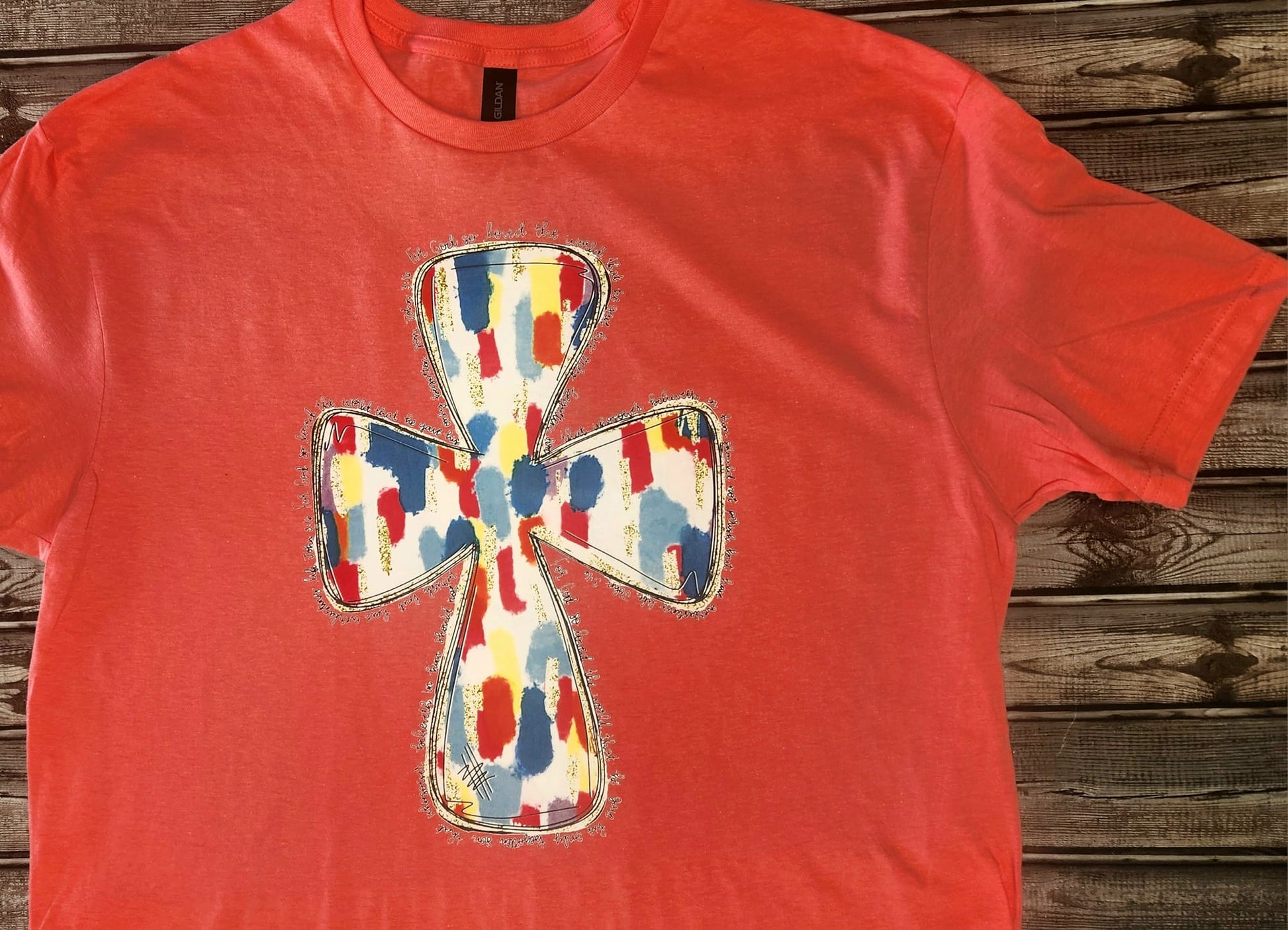 For God So Loved The World t-shirt with colorful cross design on red fabric.