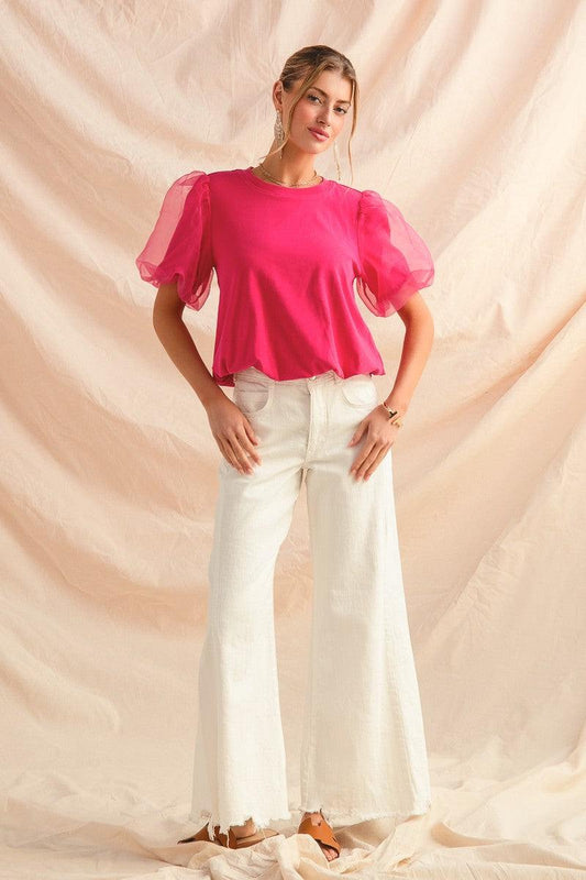 Woman wearing crisp white wide flare bottom denim pants with a bright pink puff sleeve top