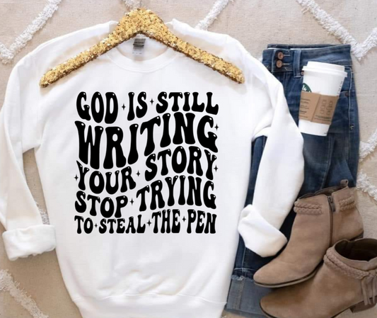 Gildan sweatshirt with "God Is Still Writing Your Story" message in black print.