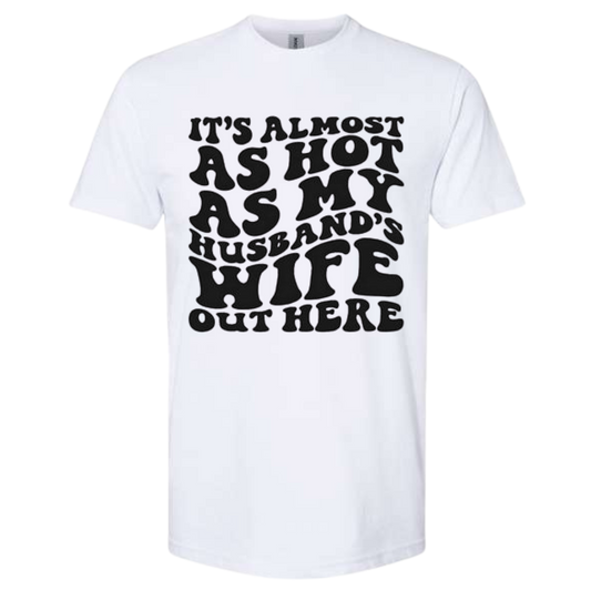 Quirky T-shirt with "It's Almost As Hot As My Husband's Wife Out Here" text.