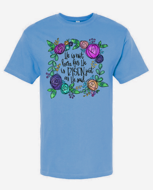 Christian blue T-shirt design featuring "He Is Not Here For He is Risen" text with colorful floral pattern.