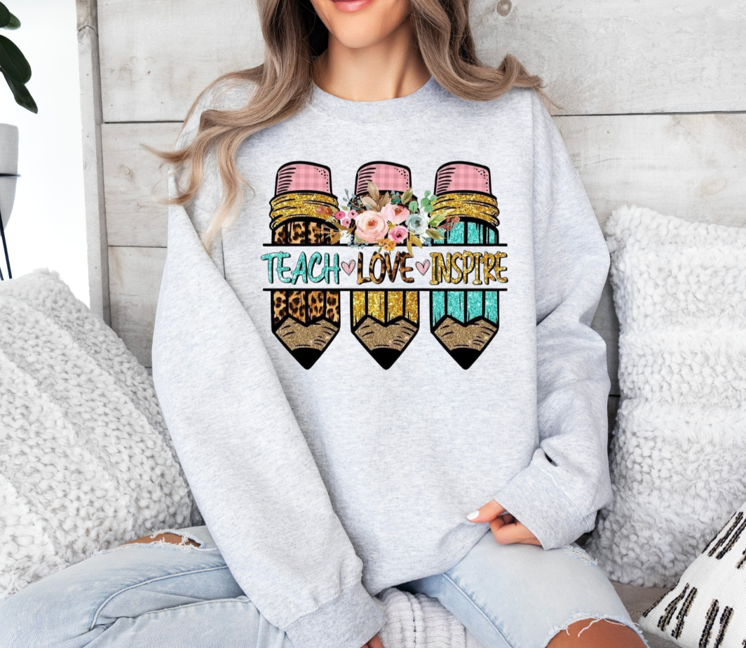 Teach Love Inspire sweatshirt, Gildan brand, featuring colorful pencil design with floral accents.