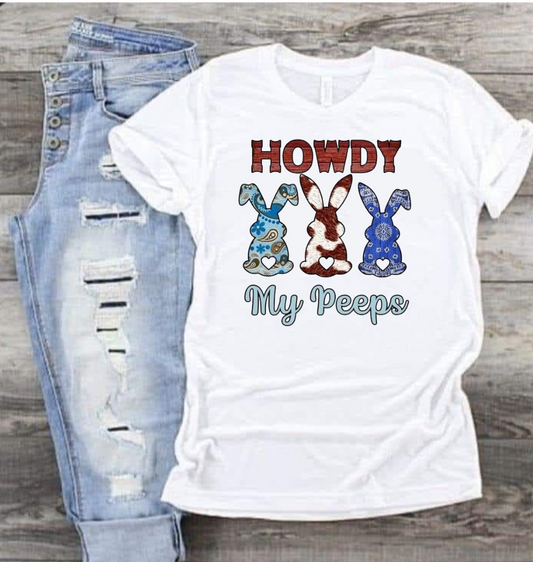 Howdy My Peeps shirt with playful bunny graphic design and text, laid beside ripped jeans.