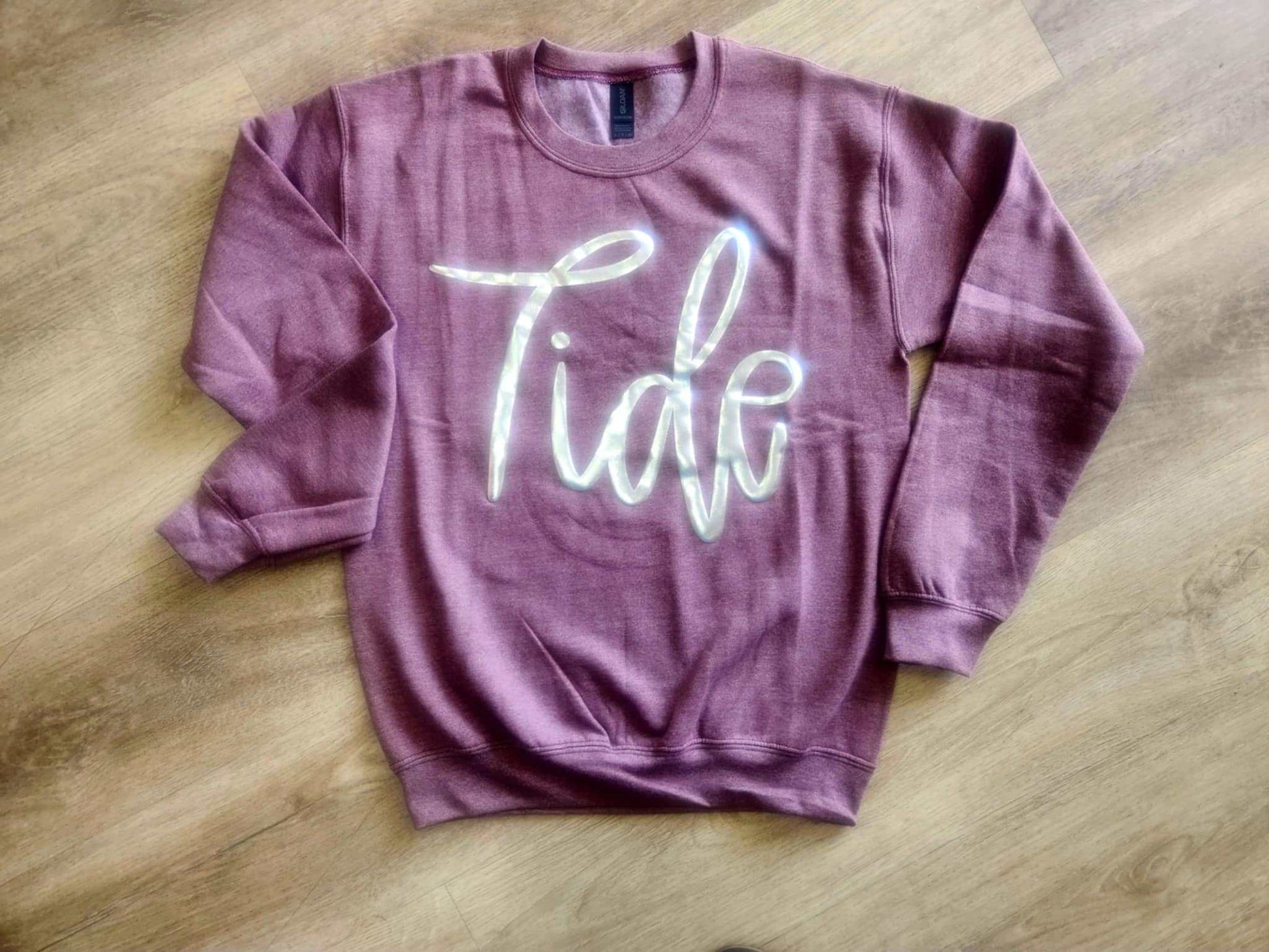 Purple Tide Jumbo Puff Sweatshirt with silver metallic logo and oversized fit on wooden floor background