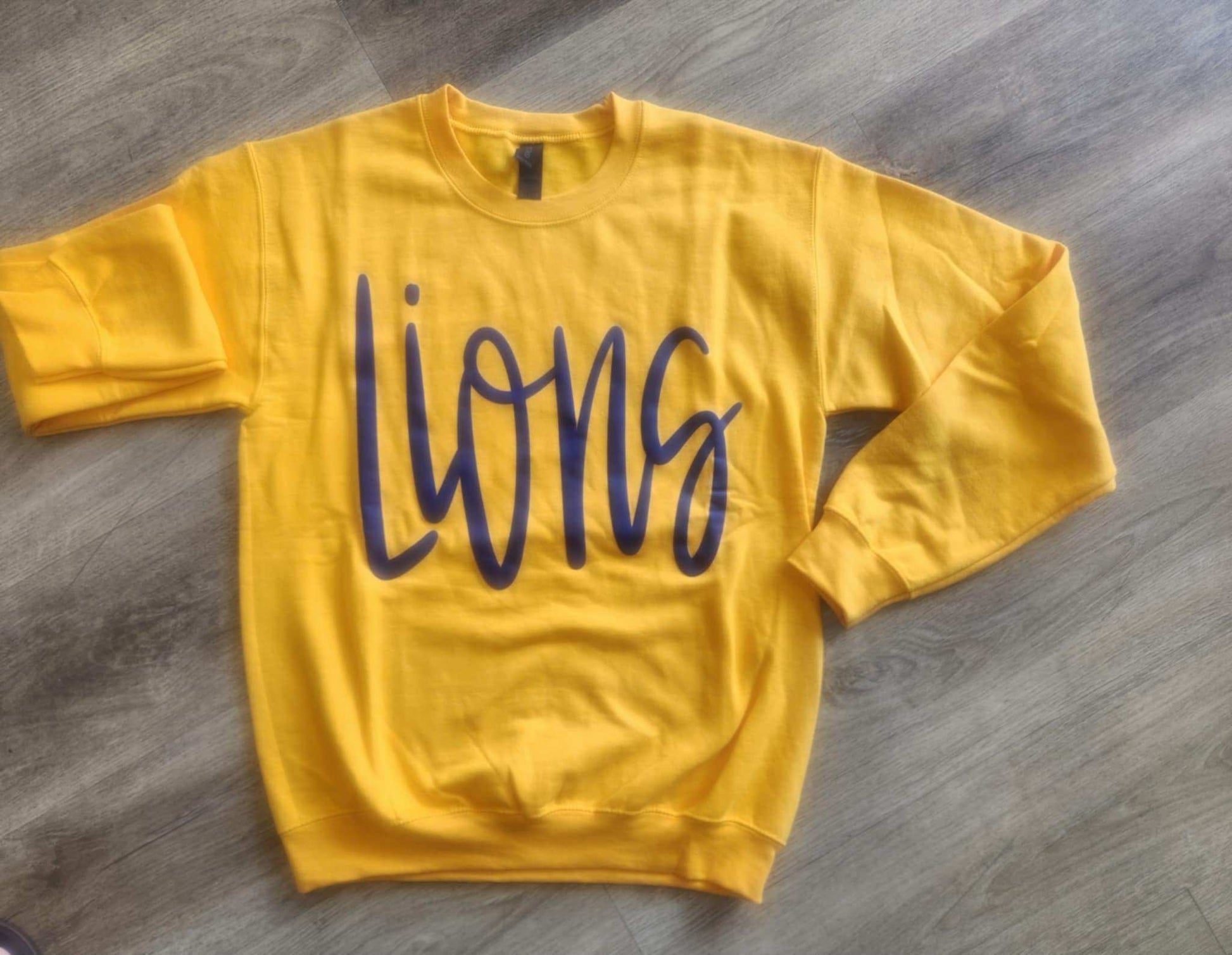 Yellow Lions Jumbo Puff Sweatshirt with bold navy lettering laid flat on wooden floor