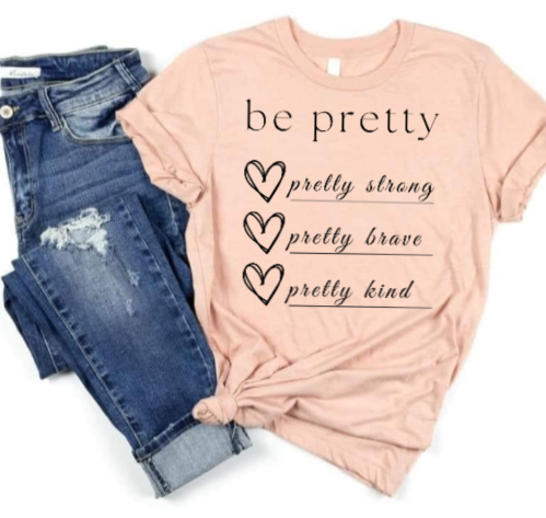 Be Pretty Strong Brave Kind shirt with heart designs, paired with jeans.